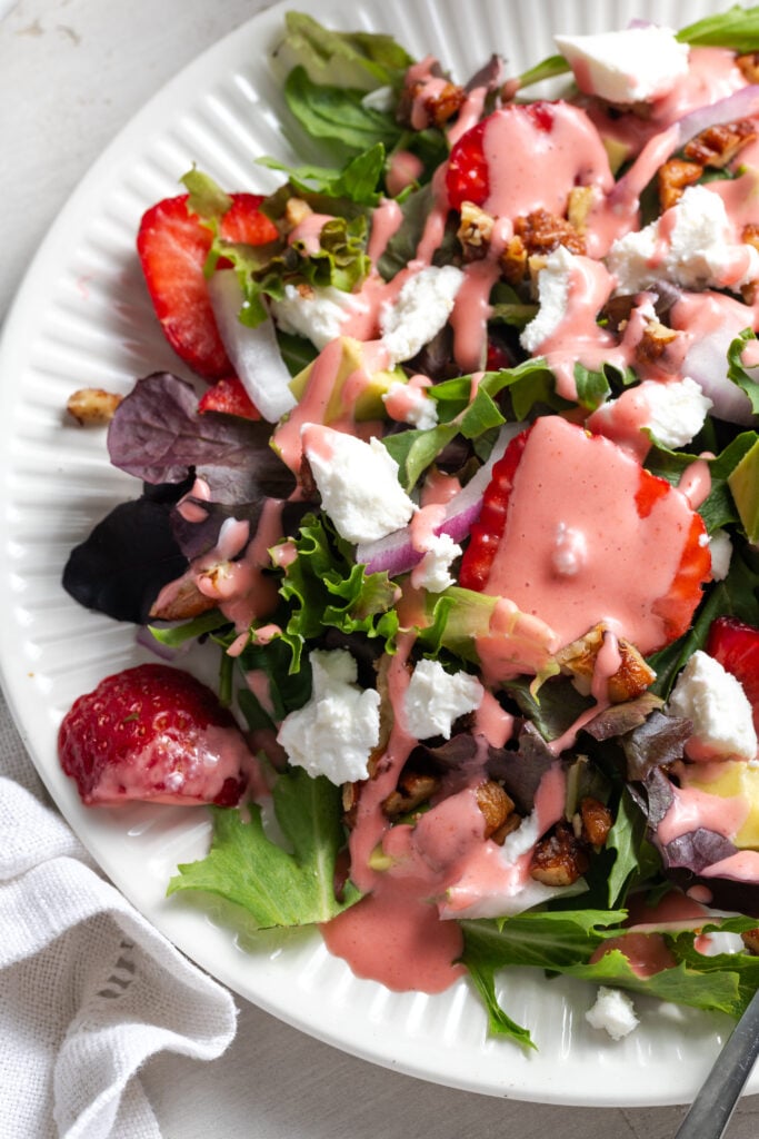 left 3/4 of a salad plate with strawberry and goat cheese salad drizzled with pale pink strawberry salad dressing.
