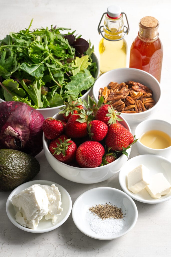 ingredients for making strawberry and goat cheese salad with candied pecans measured out on a white table.