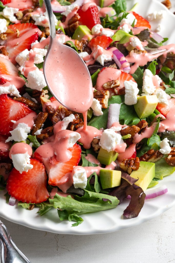 silver spoon drizzling strawberry vinaigrette on top of a serving platter with strawberry summer salad.
