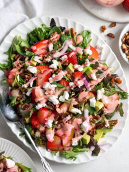 oval serving platter with strawberry salad with goat cheese crumbles, candied pecans, strawberry vinaigrette, and red onions.