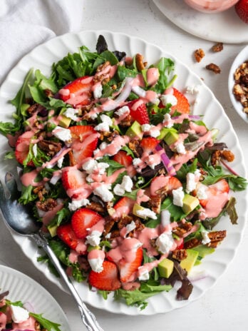 oval serving platter with strawberry salad with goat cheese crumbles, candied pecans, strawberry vinaigrette, and red onions.