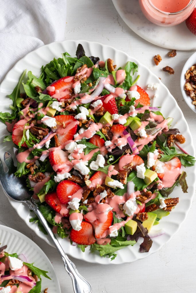 oval serving platter with strawberry salad with goat cheese crumbles, candied pecans, strawberry vinaigrette, and red onions.