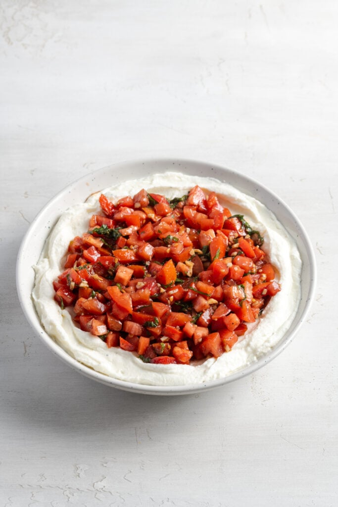 assembled bruschetta dip in a serving bowl with the whipped ricotta on bottom and tomato mixture on top.