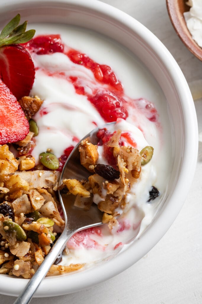 closeup shot of a white bowl filled with yogurt topped with grain free granola, fresh strawberries, and strawberry chia jam.
