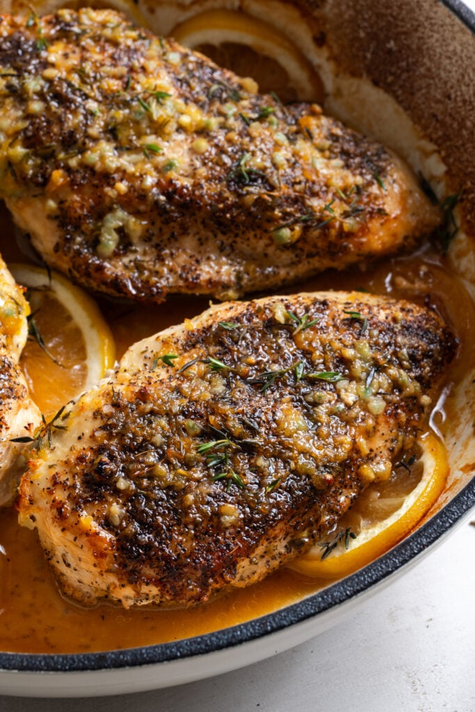 freshly baked lemon pepper chicken breast in a pan after sprinkling on some fresh thyme leaves as garnish.