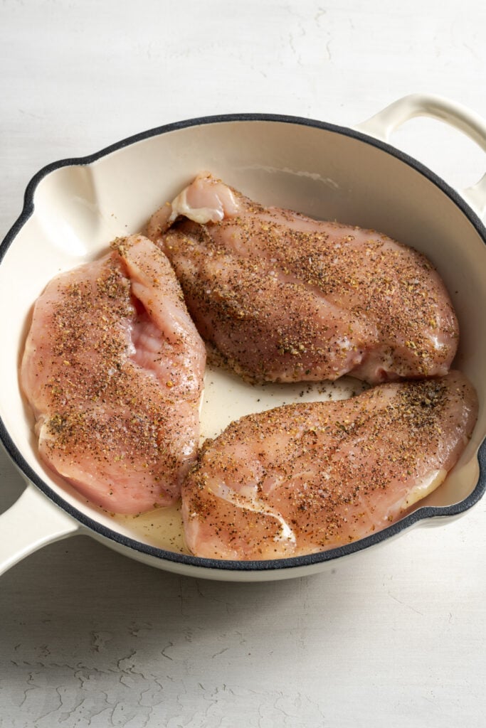 raw seasoned lemon pepper chicken breasts in a skillet browning in oil.