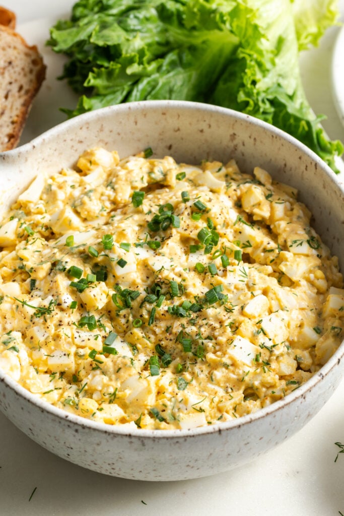 white earthenware bowl filled with cottage cheese egg salad with a head of leaf lettuce in the background.