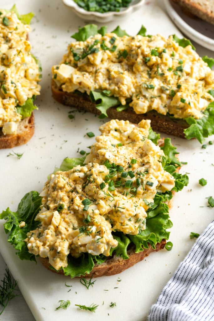 overhead view of a cutting board after putting the cottage cheese egg salad on top of toast and lettuce.