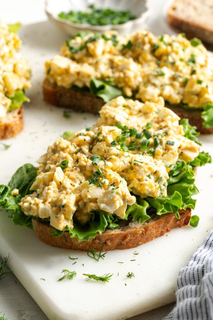open faced cottage cheese egg salad sandwiches on a white cutting board.