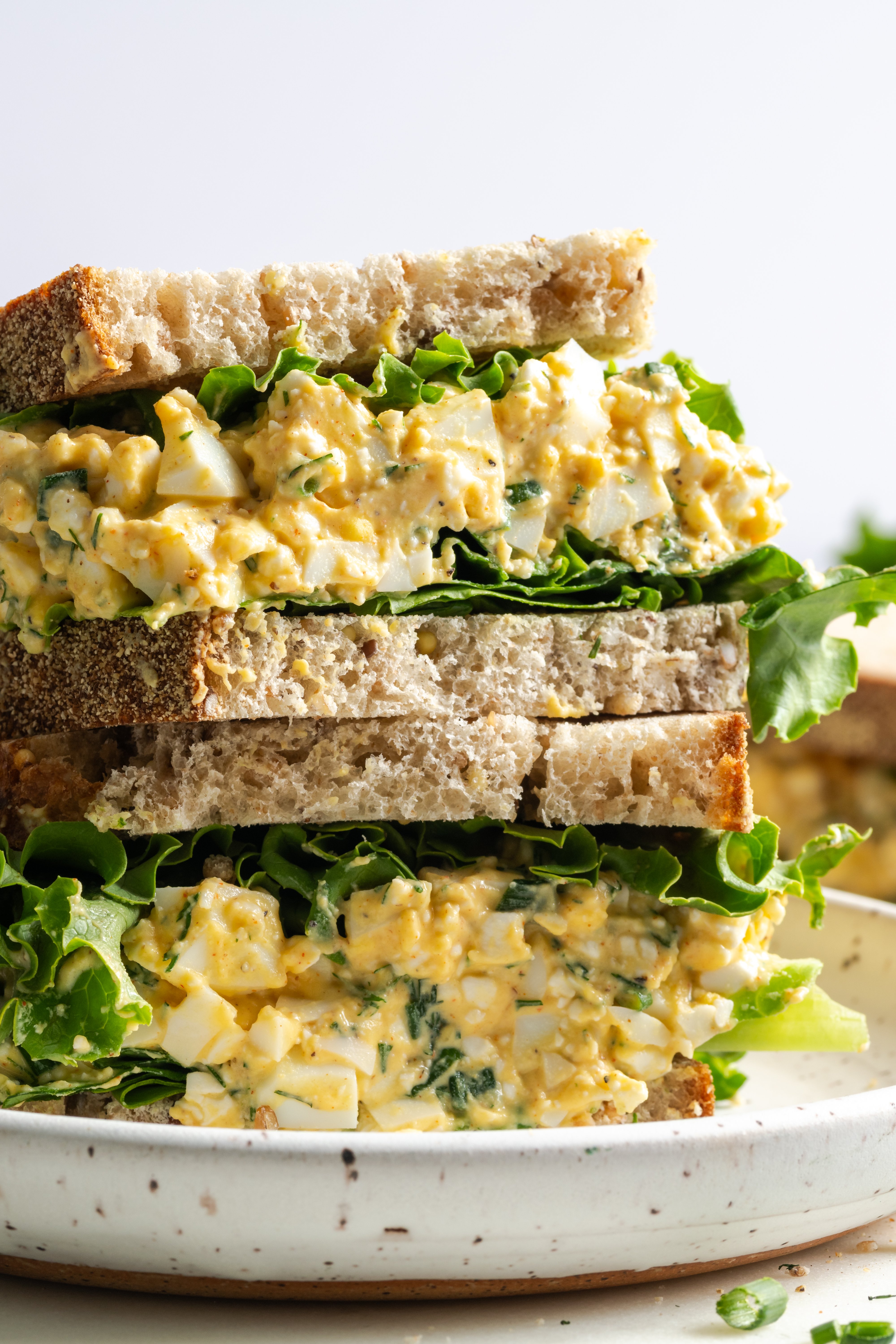 egg salad cottage cheese sandwich that has been halved and stacked on a white earthenware plate.
