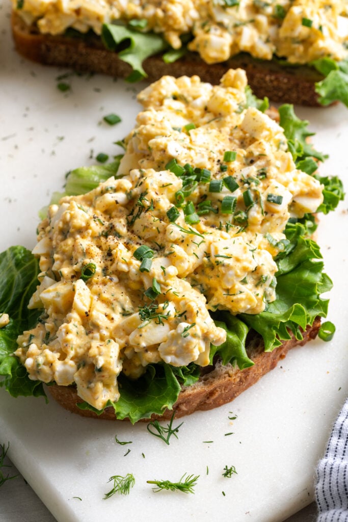 healthy egg salad with cottage cheese served on multigrain toast with a lettuce leaf and topped with fresh chives and dill.