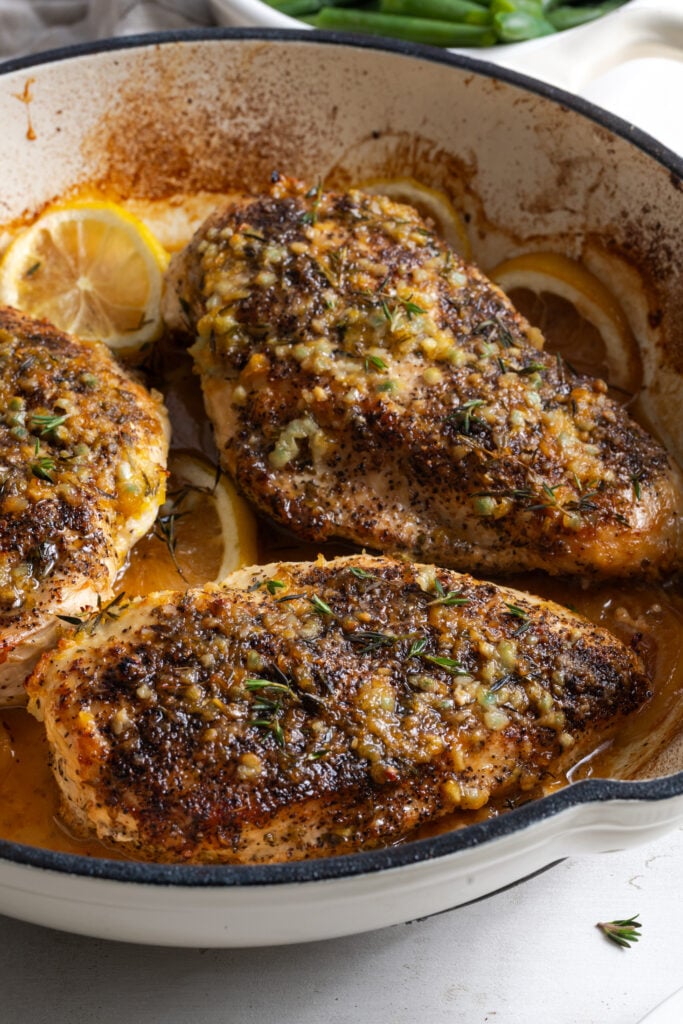 45 degree angle closeup shot of lemon pepper chicken breasts in a deep, white enameled skillet after baking.