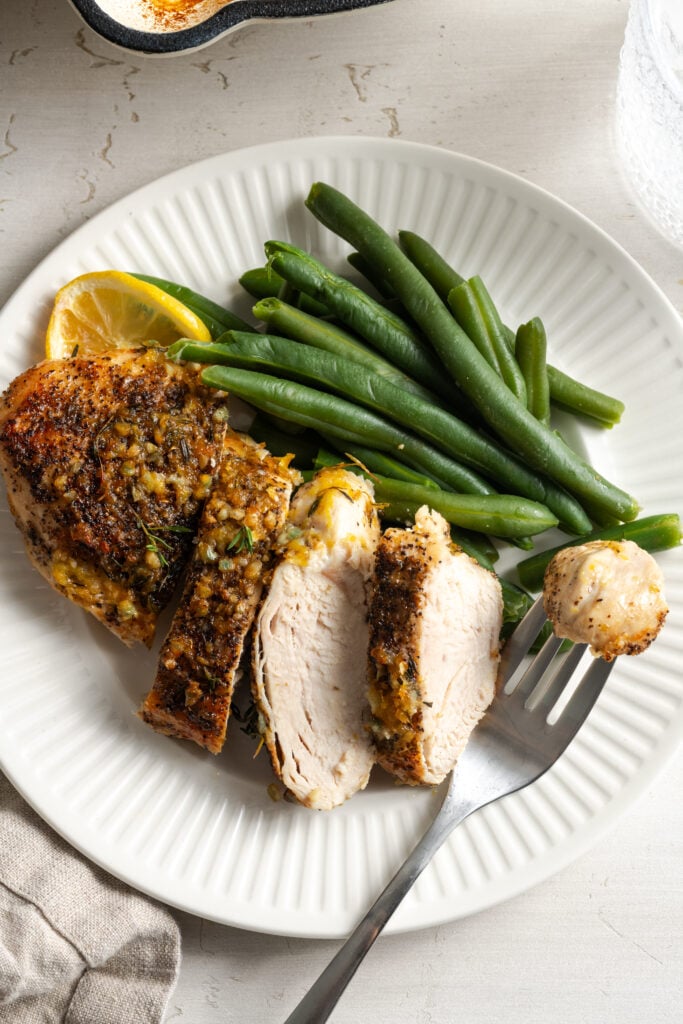 dinner plate with oven baked lemon pepper chicken breast, thinly sliced lemon, and crisp steamed green beans.