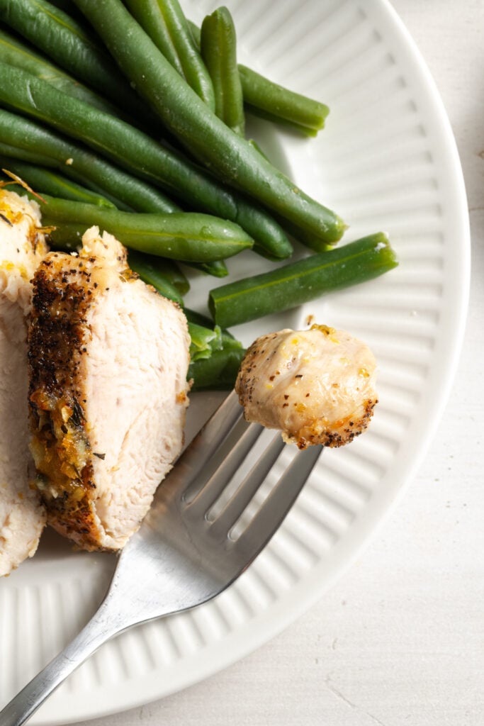 closeup shot of a bite of lemon pepper chicken on a plate with green beans; the meat is well browned on the outside, but looks juicy on the inside.