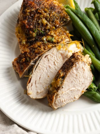 closeup shot of an oven baked lemon pepper chicken breast on a white plate after being sliced and served with steamed green beans.
