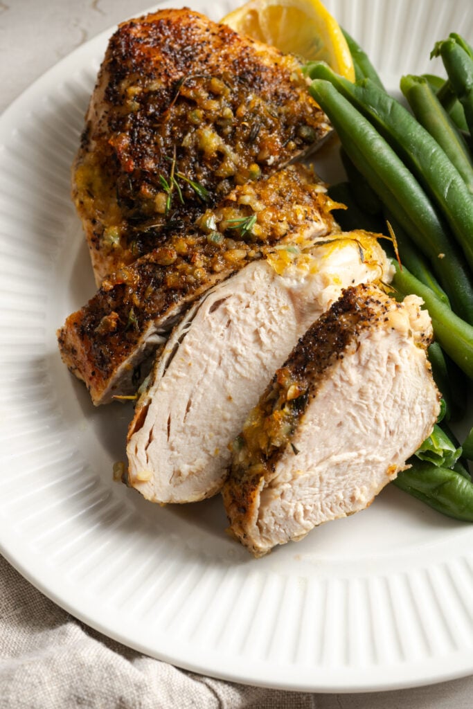 closeup shot of an oven baked lemon pepper chicken breast on a white plate after being sliced and served with steamed green beans.