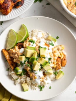 overhead shot of a street corn chicken rice bowl topped with avocados, crema, and lime slices.