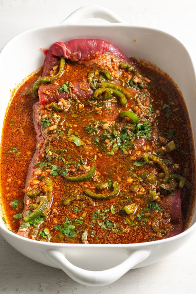 flank steak marinating in a white dish.