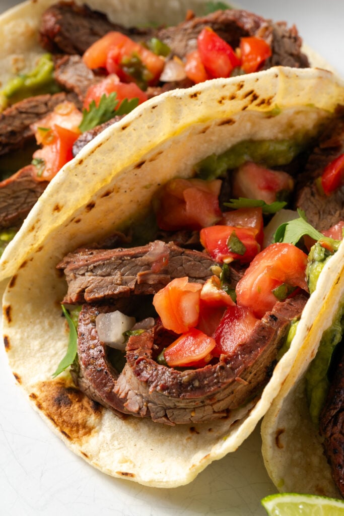 closeup shot of a few flank steak tacos topped with pico de gallo and cilantro.