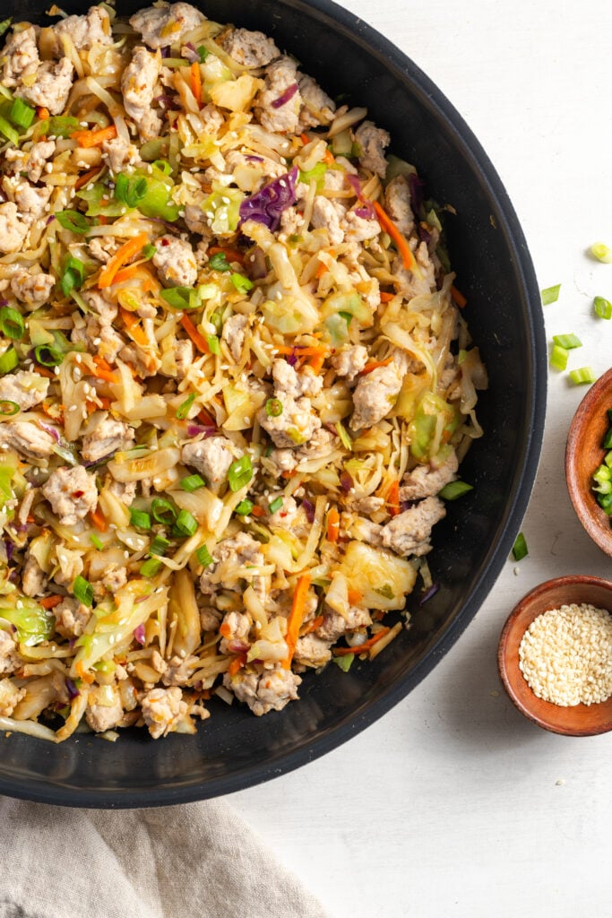 closeup shot of healthy turkey egg roll in a bowl cooking in a black skillet on a white table with scallions scattered around.