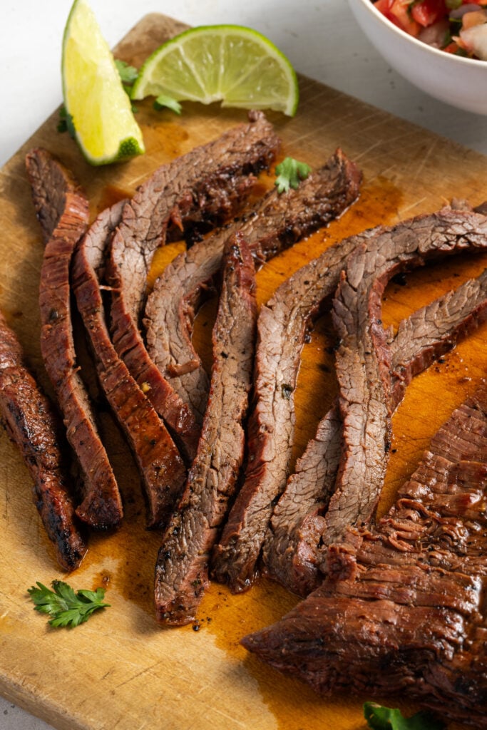 marinated and cooked flank steak on a wooden cutting board after resting and slicing.