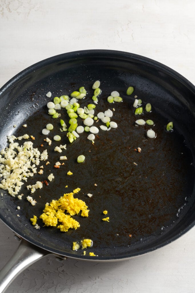 scallion whites and pale greens, ginger, and garlic sautéing in a pan with oil.