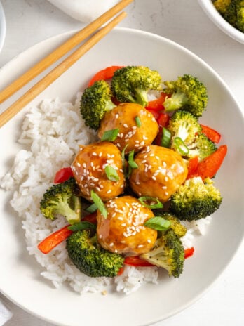 plate of chicken meatballs with roasted veggies tossed in a pineapple teriyaki sauce over a bed of steamed white rice with a pair of chopsticks.