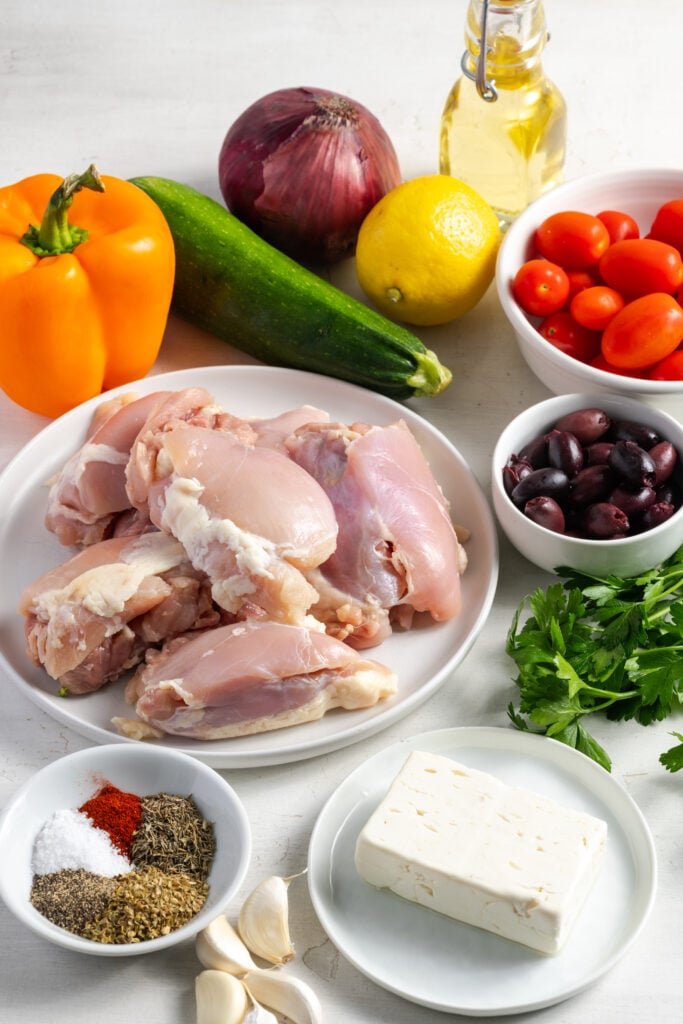ingredients for making greek sheet pan chicken recipe measured out on a white table.