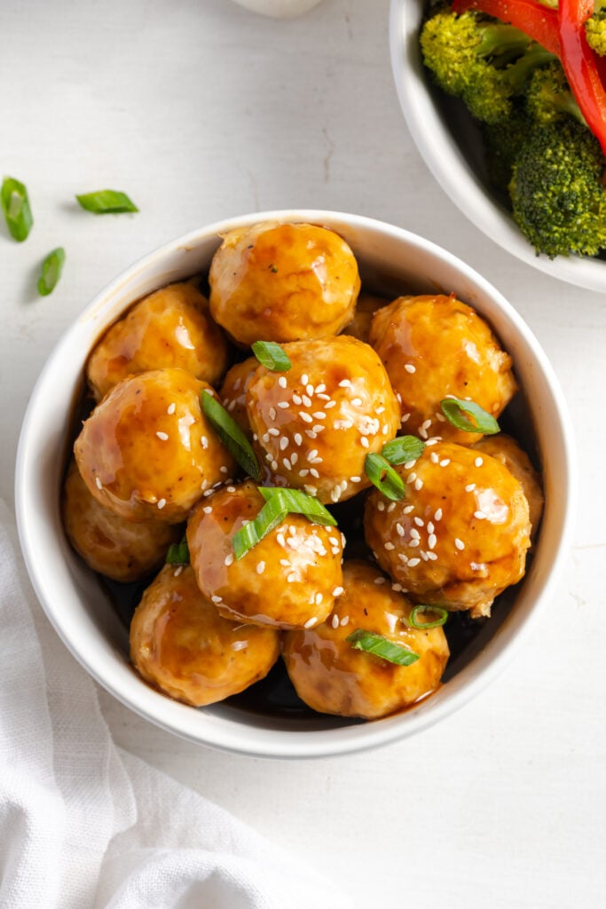 white bowl filled with homemade pineapple teriyaki chicken meatballs coated in a sticky sweet glaze and topped with scallions and sesame seeds.