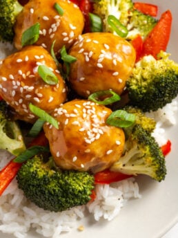 hyper closeup shot of pineapple and teriyaki chicken meatballs in a bowl showing their sticky sweet glaze and garnished with sesame seeds and green onions.