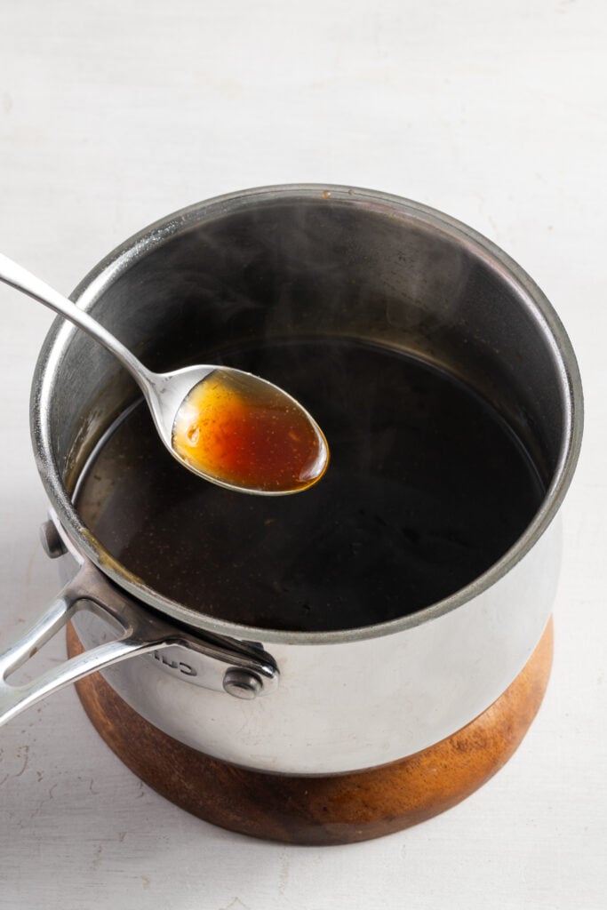 silver spoon taking a spoonful of homemade pineapple teriyaki sauce from a steaming saucepan.