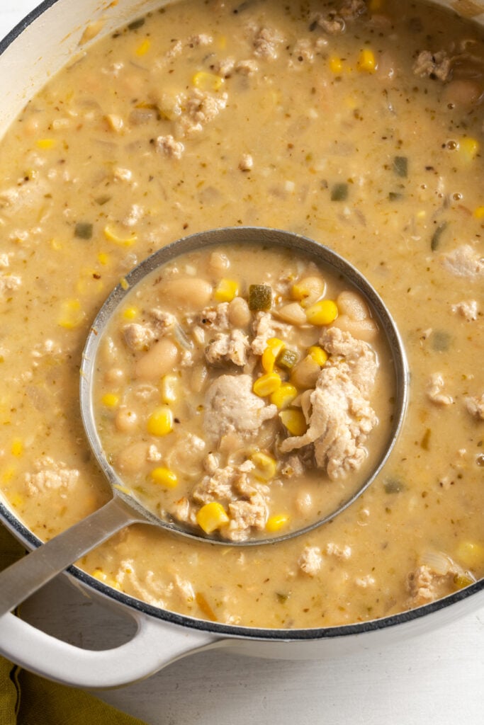 overhead shot of a silver ladle taking a portion of white turkey chili from the white dutch oven.