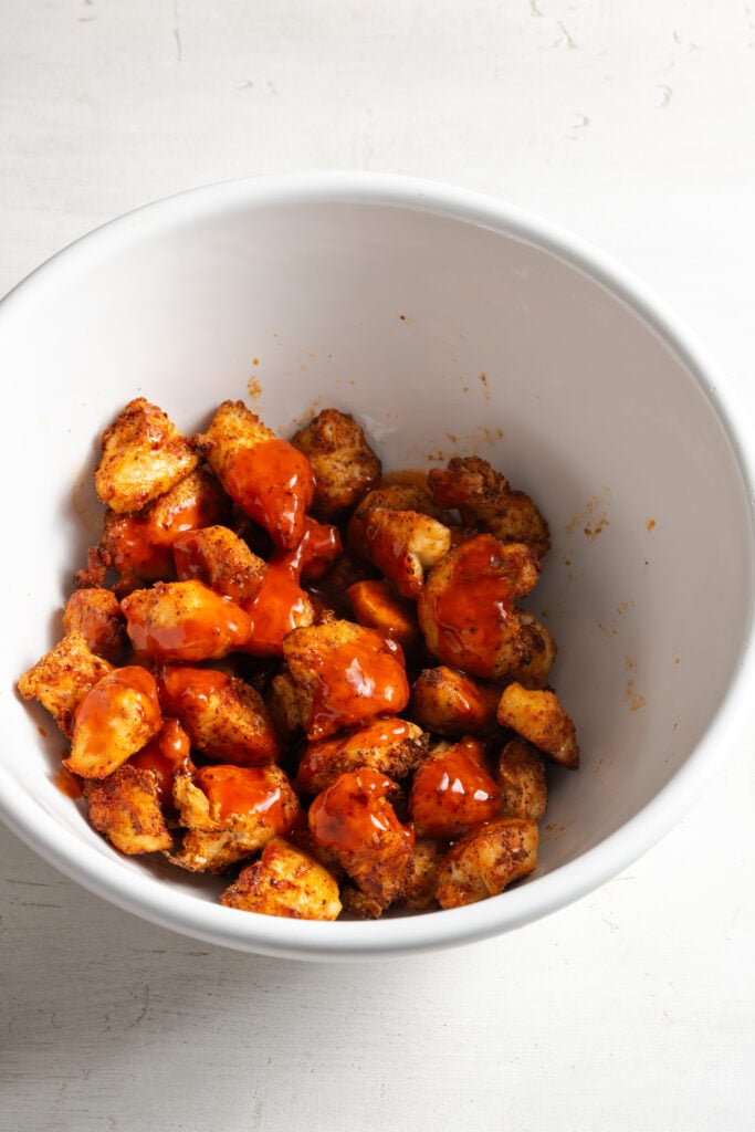buffalo sauce added to the air fried chicken breast bites in the mixing bowl.
