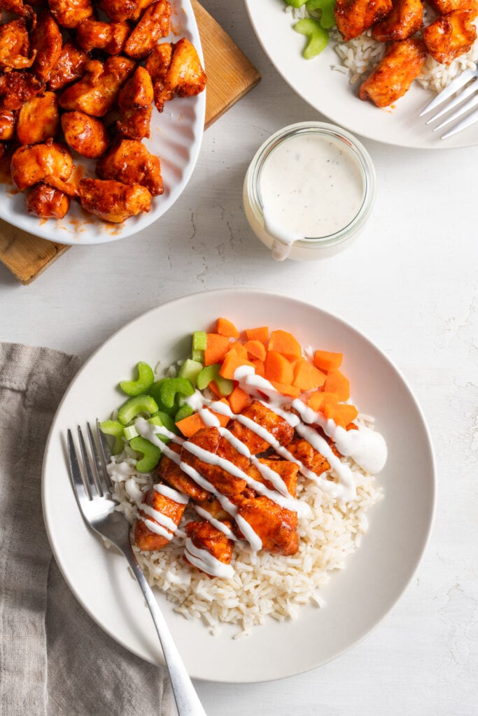 flat lay shot of two air fryer buffalo chicken bites rice bowls with the platter with the rest of the chicken bites to the side.