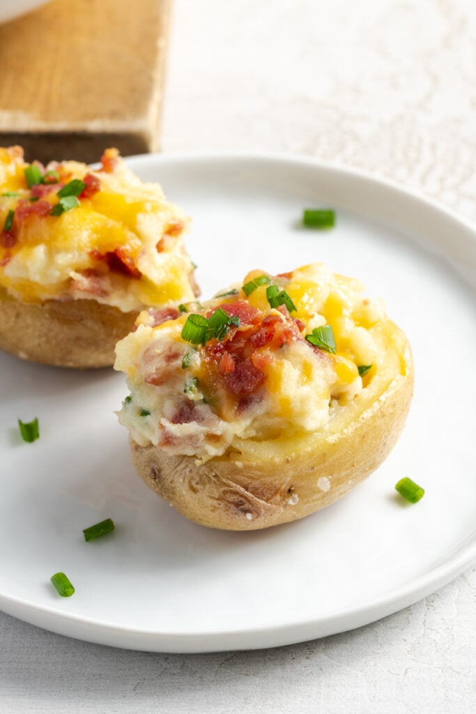 white appetizer plate with two twice baked mini potatoes topped with fresh chives.