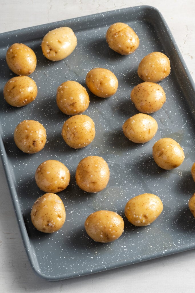 baby potatoes that have been tossed in oil and salt on a grey baking sheet.