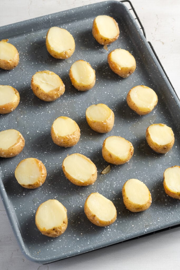 baked baby potatoes on a baking sheet with their tops sliced off to scoop out the innards.