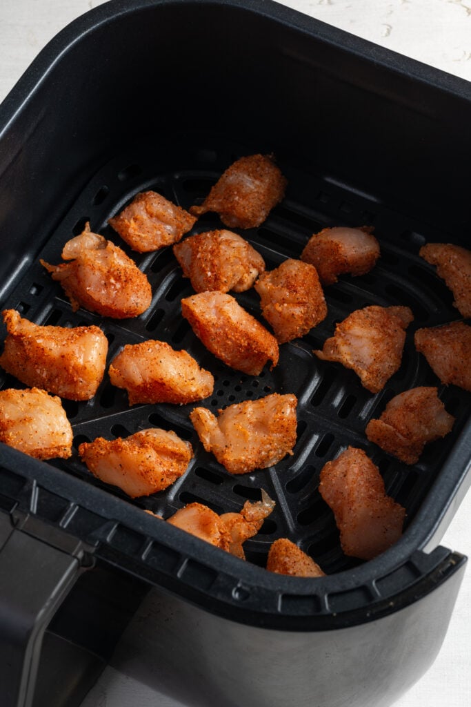 raw buffalo chicken bites in the basket of an air fryer.