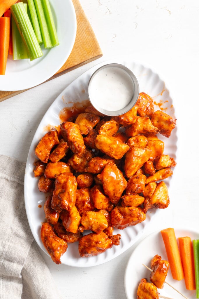 overhead shot of a white oval serving plate of air fried buffalo chicken bites with a dipping bowl of ranch and a separate white plate with celery and carrot sticks.