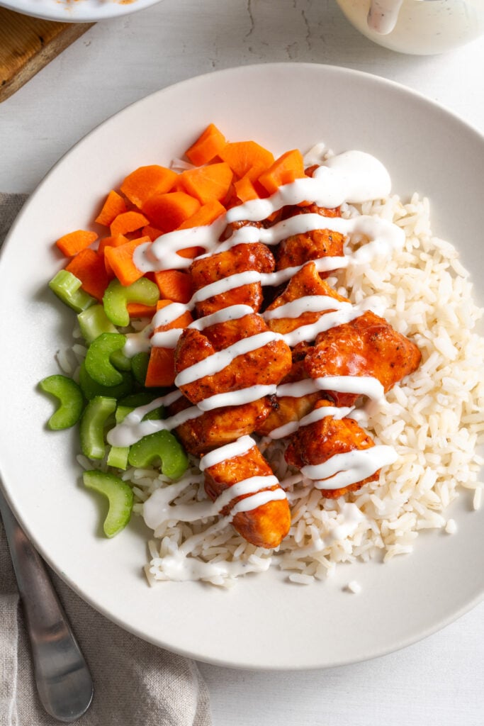 flat lay shot of air fryer buffalo chicken bites rice bowl with chopped veggies and ranch dressing.