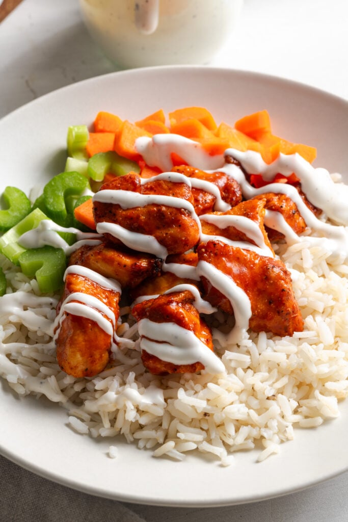 boneless buffalo chicken bites on a bed of rice with chopped veggies and a drizzle of ranch.