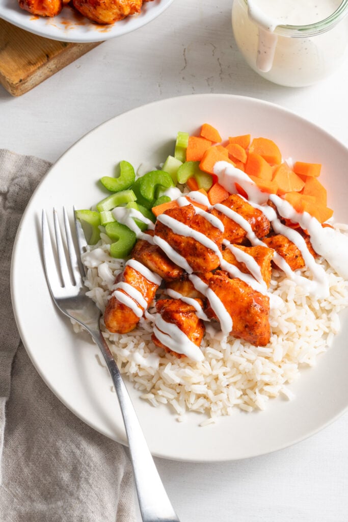 air fried buffalo chicken bites with rice, veggies, and ranch dressing on a white plate with a silver fork.