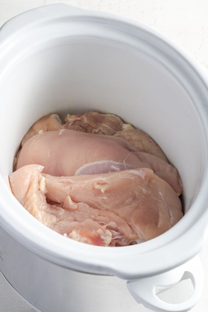 raw chicken breasts added to a slow cooker.