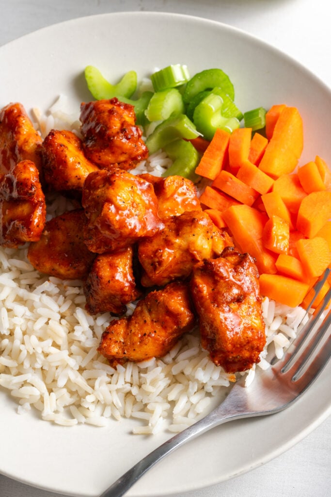 closeup shot of a white dinner plate with white rice, a scoop of buffalo chicken bites, and chopped celery and carrots.