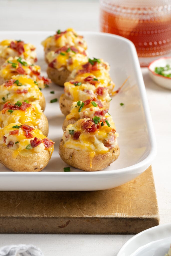 rectangular white serving platter with mini baked potatoes with a cocktail glass blurred out in the background.