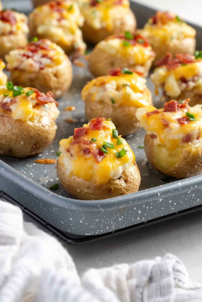 45 degree angle shot of a grey baking sheet with mini baked potatoes after stuffing and baking a second time.