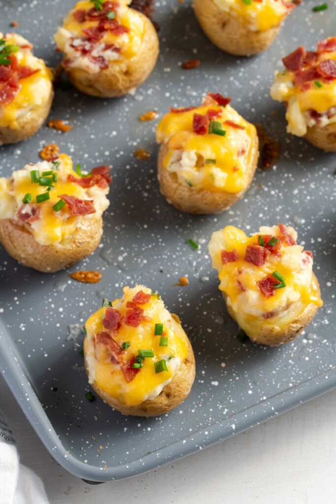 mini baked potatoes with cheese, bacon and chives on a grey baking sheet.