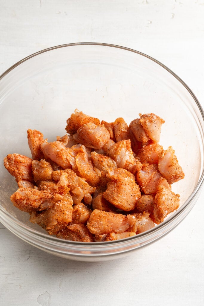 buffalo seasoned raw chicken bites in a mixing bowl.
