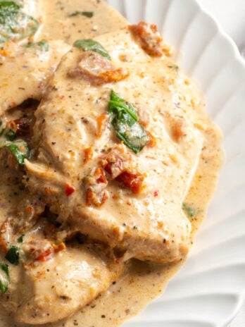 closeup shot of slow cooker tuscan chicken on a serving platter with creamy sun dried tomato and spinach sauce.