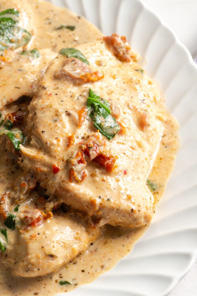 closeup shot of slow cooker tuscan chicken on a serving platter with creamy sun dried tomato and spinach sauce.